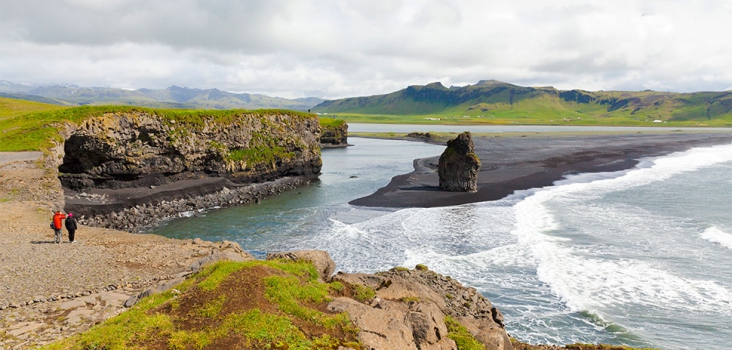 Two people walking in long distance close to a black beach in Iceland